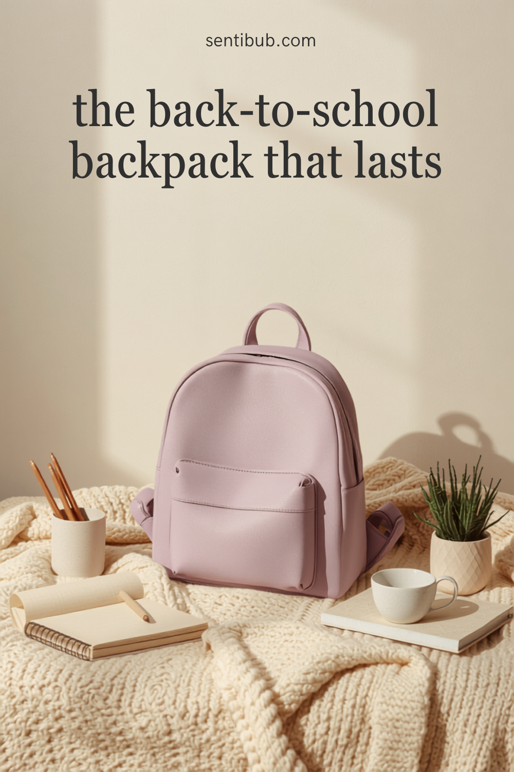 a soft mauve-lilac backpack styled on a cream knit blanket with a notebook, pens and a small plant